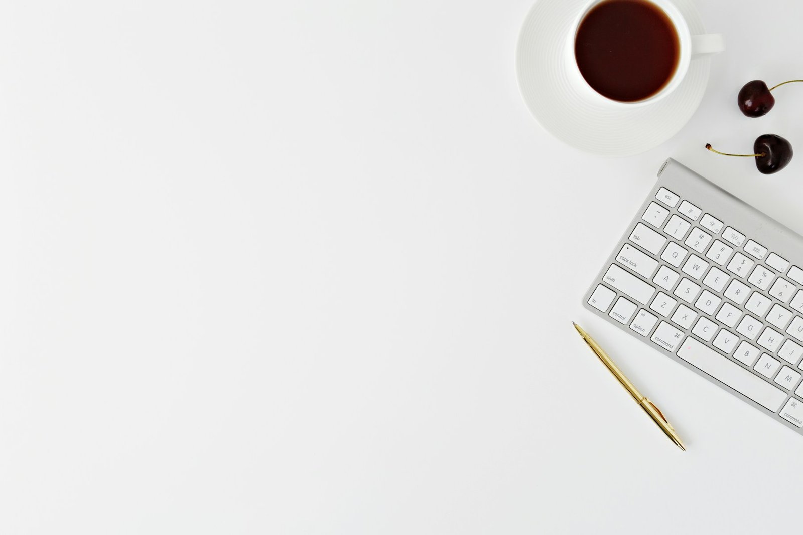 A white desktop with a keyboard, pen and coffee cup