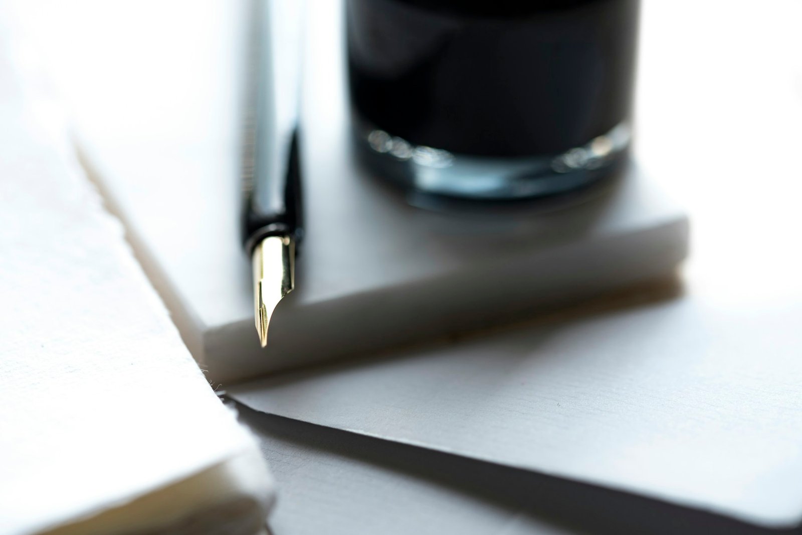 A fountain pen beside a dark ink bottle on light paper